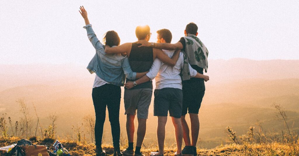 A group of friends embrace while enjoying a sunset view from the mountain top.