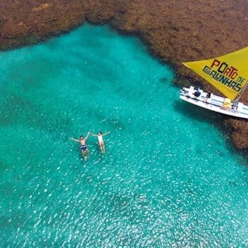 Aerial shot of people swimming near a boat in the turquoise waters of Porto de Galinhas.